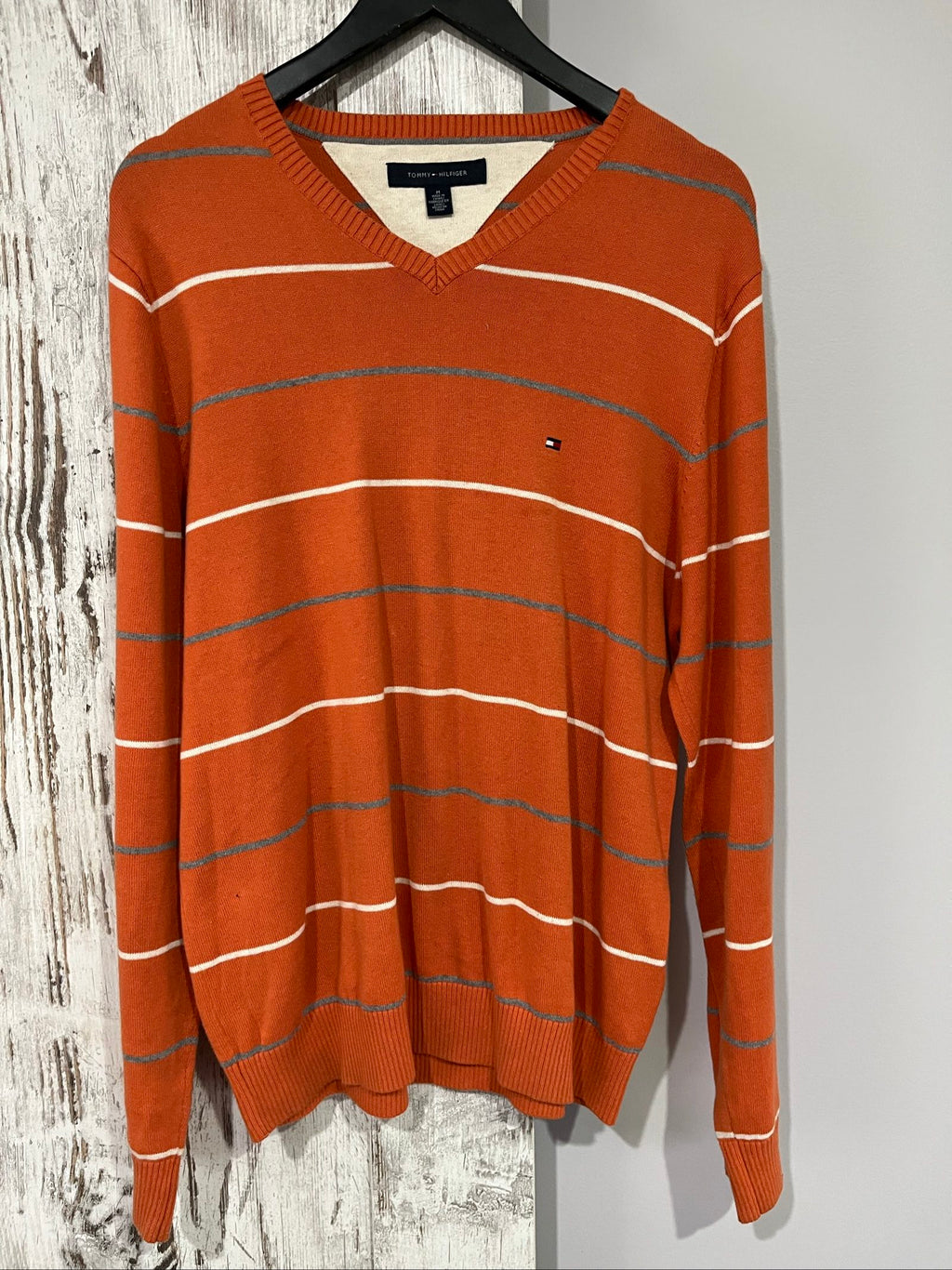 Tommy Hilfiger men's grey and white striped v-neck sweater with embroidered flag logo.