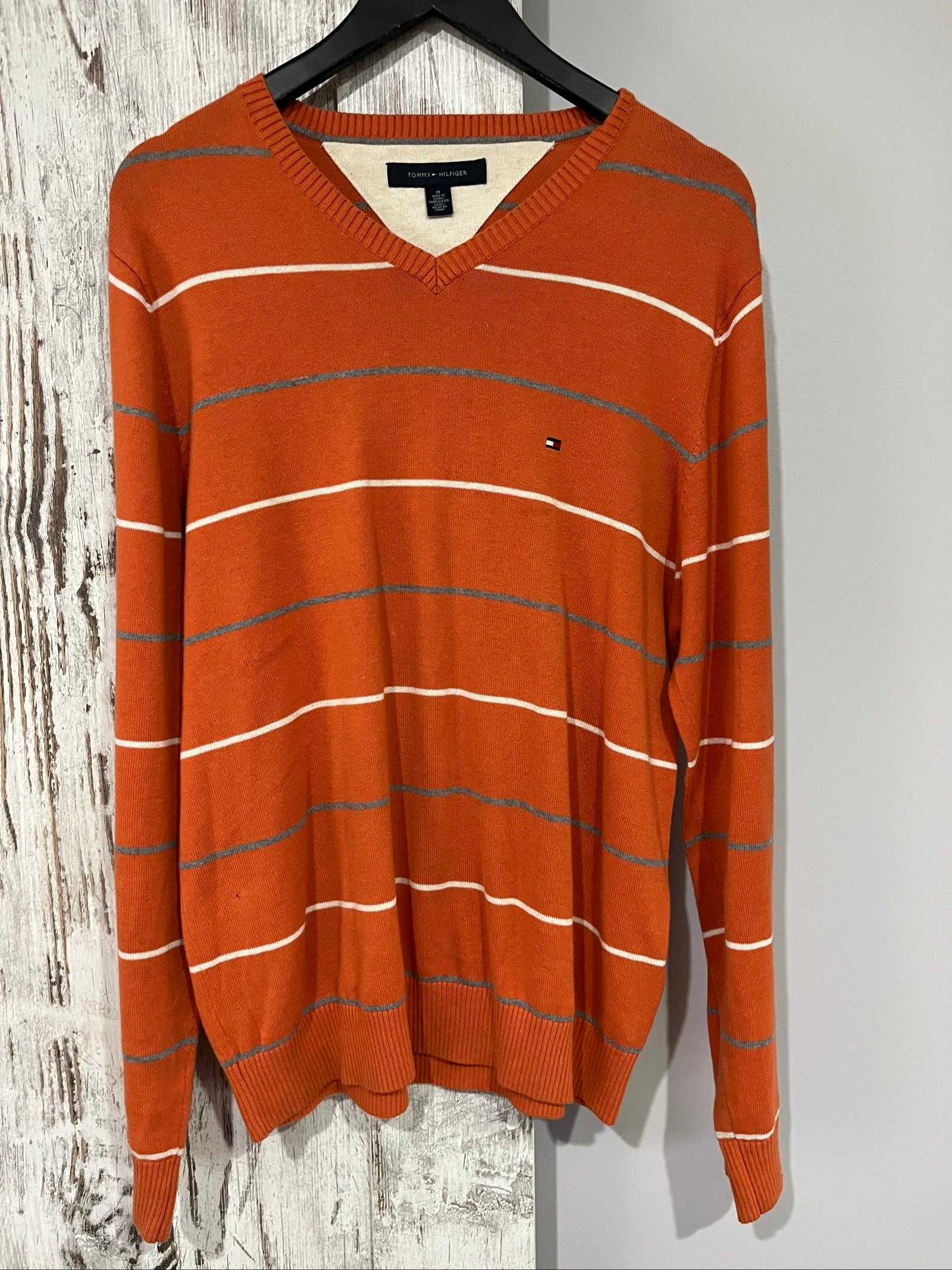 Tommy Hilfiger men's grey and white striped v-neck sweater with embroidered flag logo.