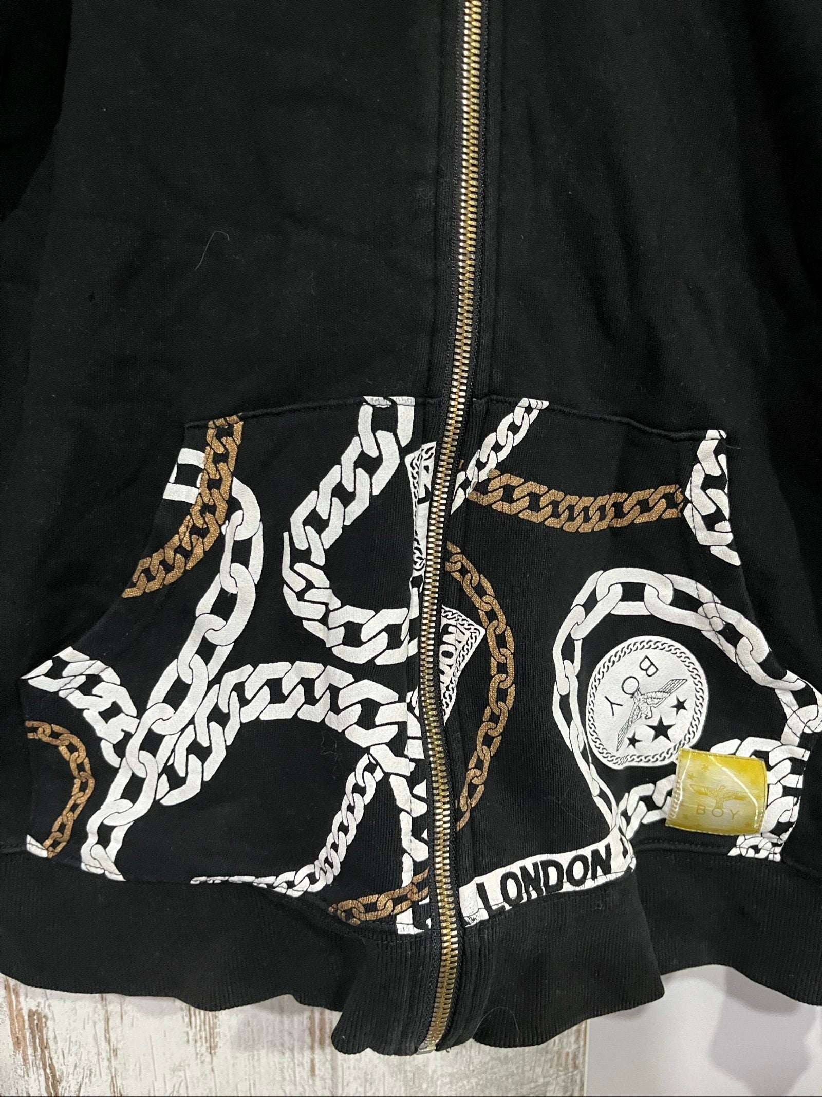 Boy London black zip-up hoodie with gold chain print and logo patch details.