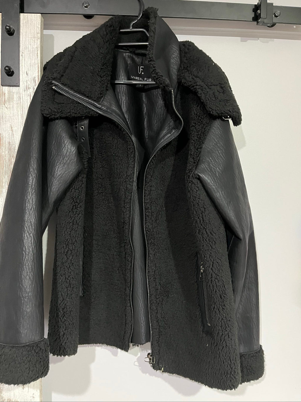 Unreal Fur black vegan shearling jacket with zip front, shearling cuffs, and buckle detail.