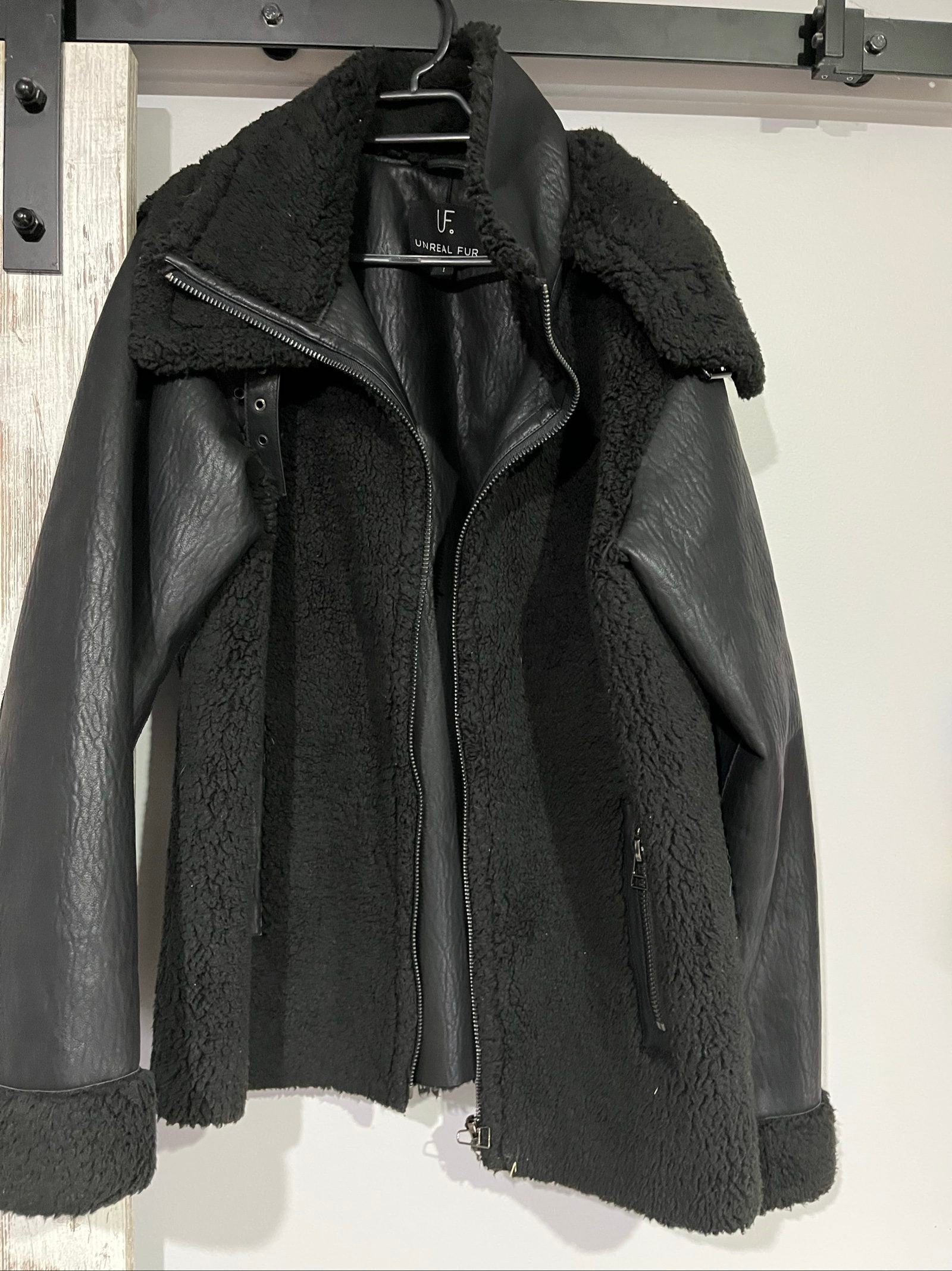 Unreal Fur black vegan shearling jacket with zip front, shearling cuffs, and buckle detail.