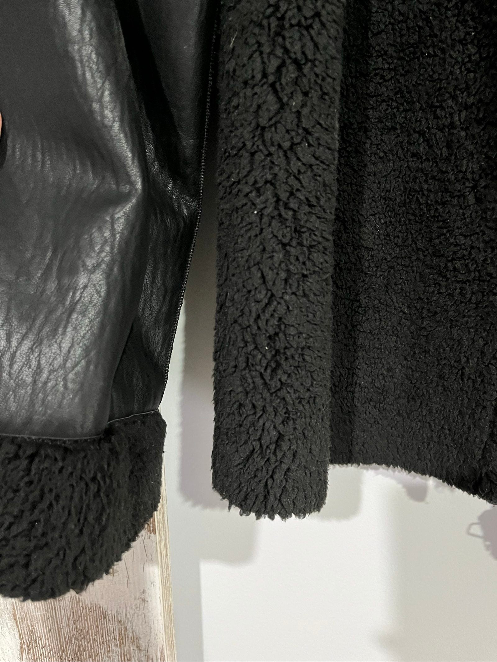 Unreal Fur black vegan shearling jacket with zip front, shearling cuffs, and buckle detail.