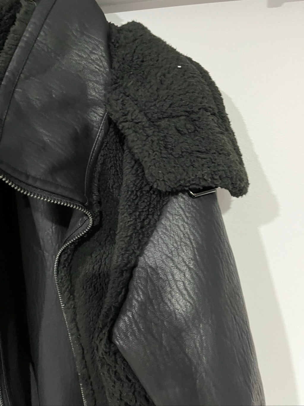 Unreal Fur black vegan shearling jacket with zip front, shearling cuffs, and buckle detail.