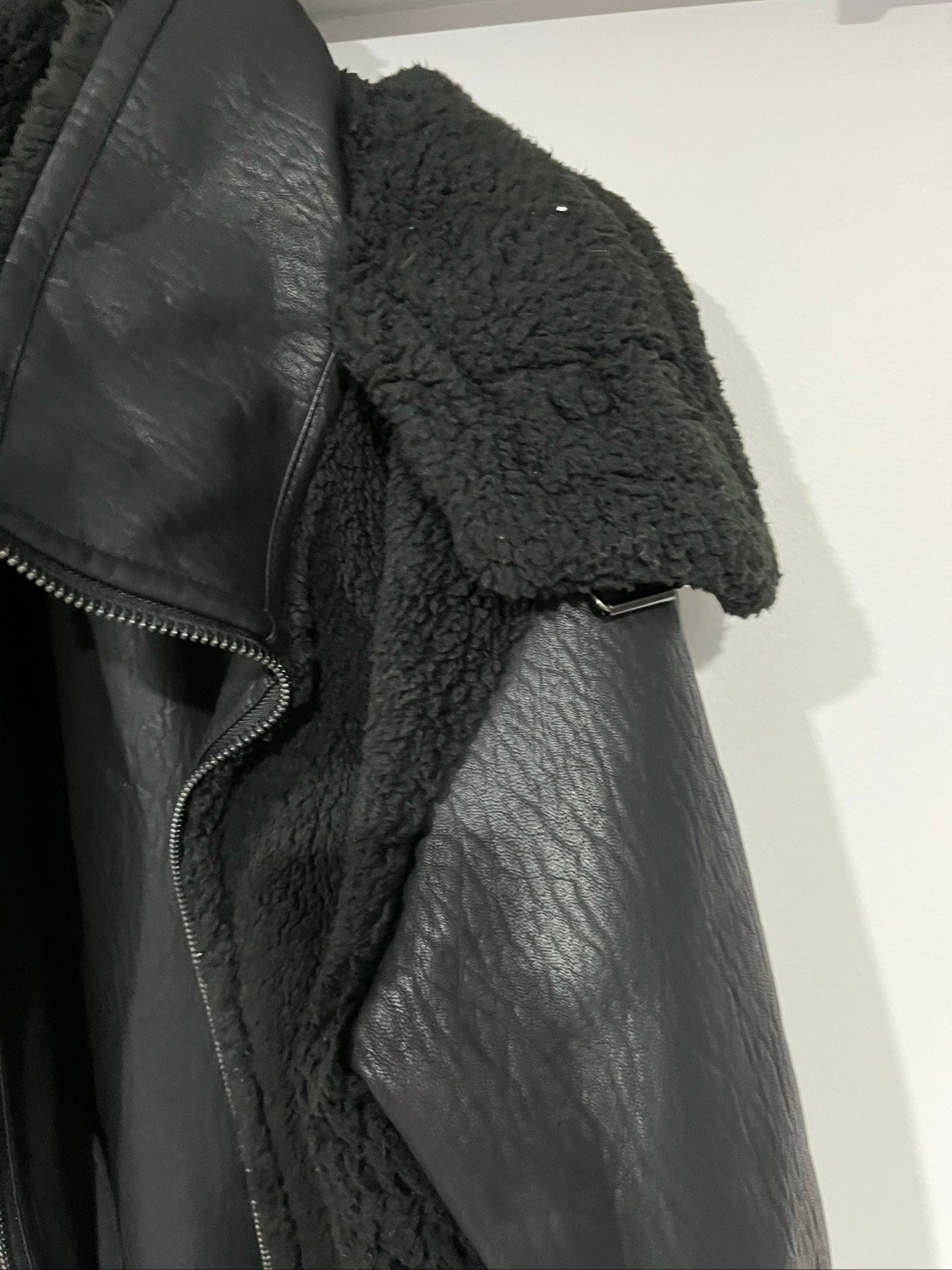 Unreal Fur black vegan shearling jacket with zip front, shearling cuffs, and buckle detail.
