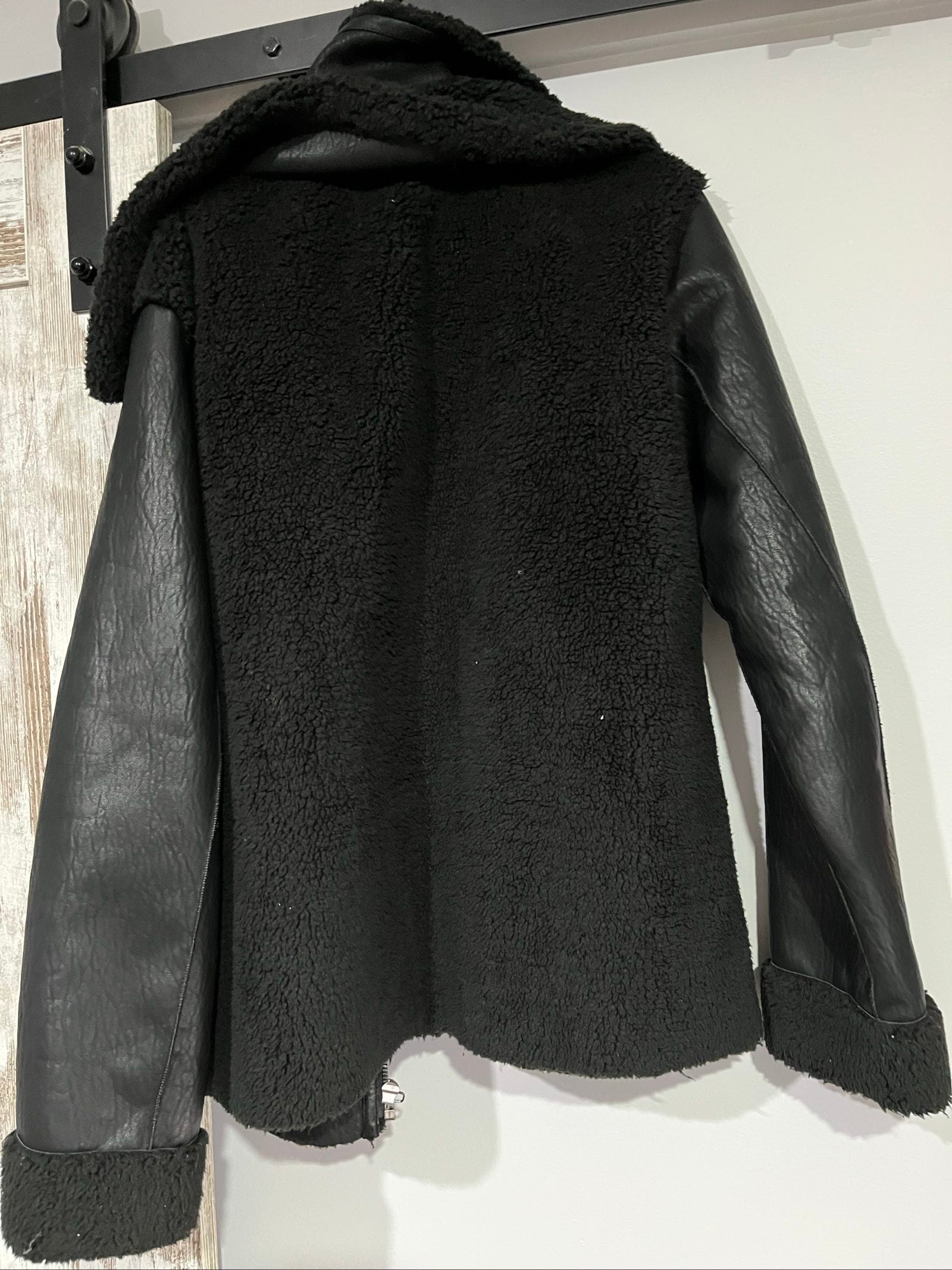 Unreal Fur black vegan shearling jacket with zip front, shearling cuffs, and buckle detail.